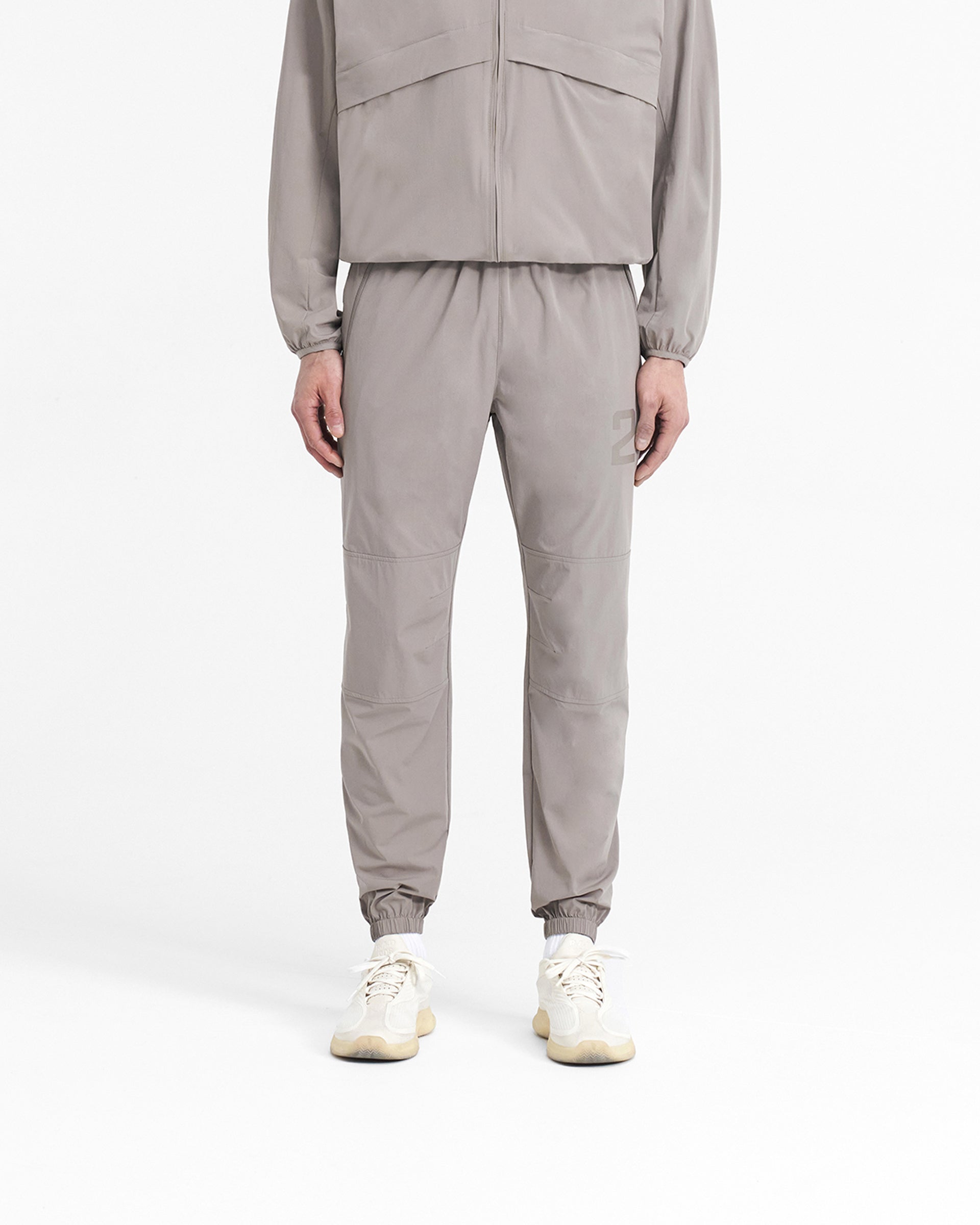 Man wearing grey training pants on a plain white background | 247 Training Pant in Cinder | Pants with elasticated waistband and zip pockets | 247 Pants | Represent Clo