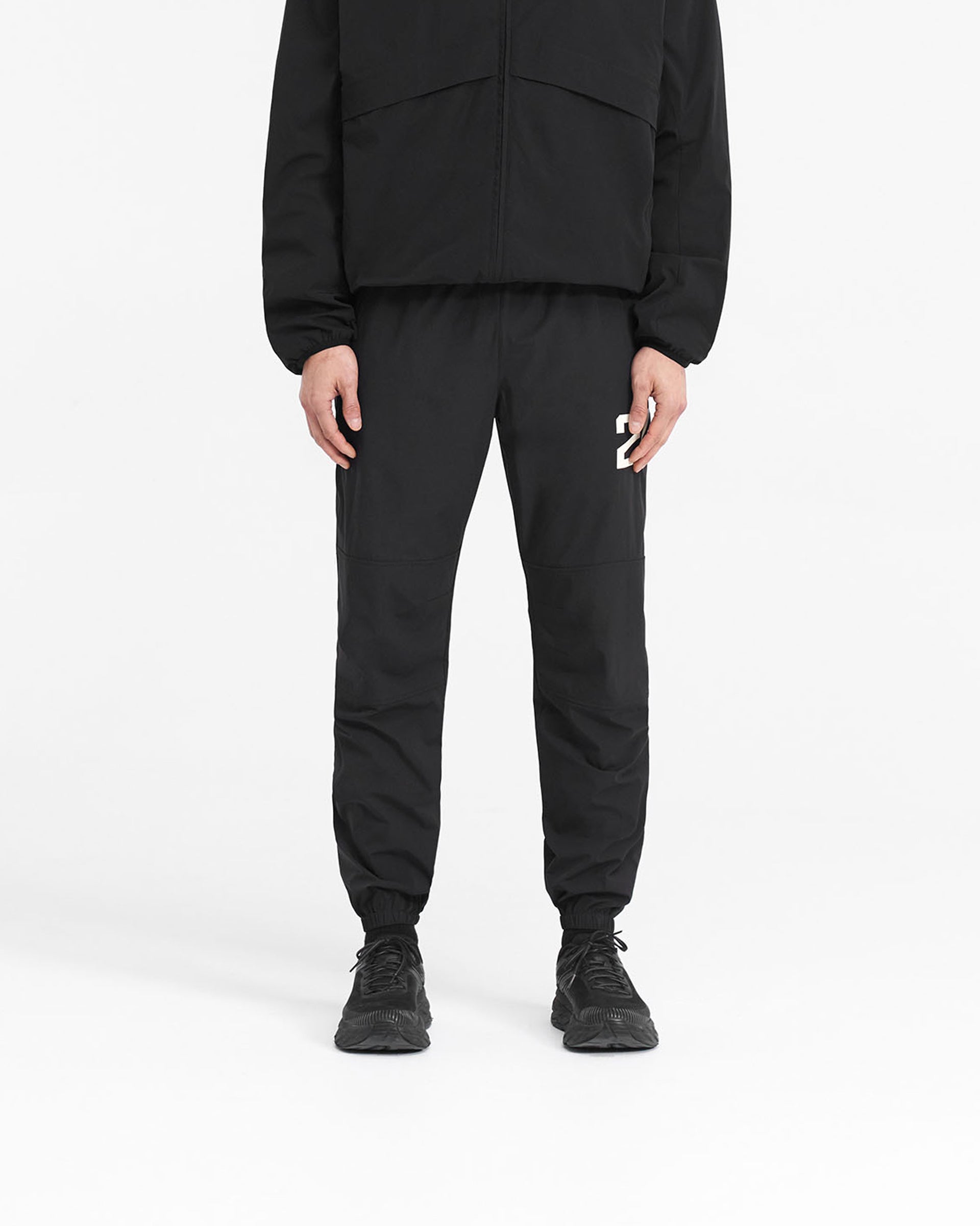 Man wearing black pants on a plain white background | 247 Training Pant in Jet Black | Training pants with zip pockets and elasticated waistband | 247 Pants | Represent Clo
