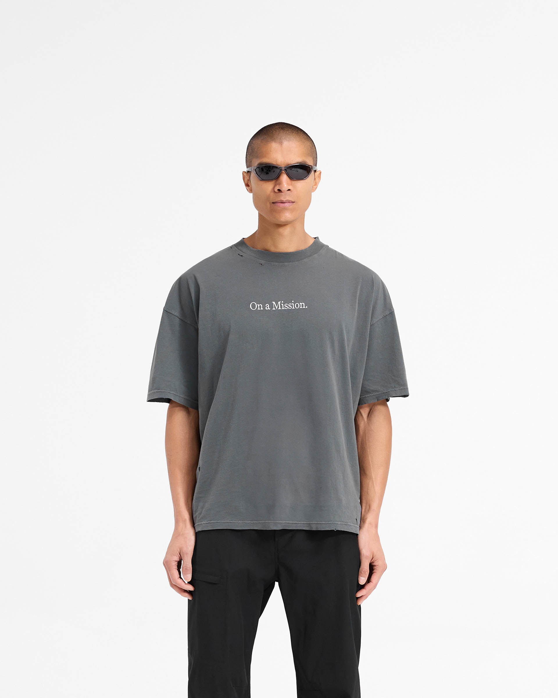 Man wearing an oversized black t-shirt on a plain white background | 247 On A Mission Oversized T-Shirt in Aged Black | T-Shirt with On a Mission embroidery and distressing details | 247 T-Shirts | Represent Clo