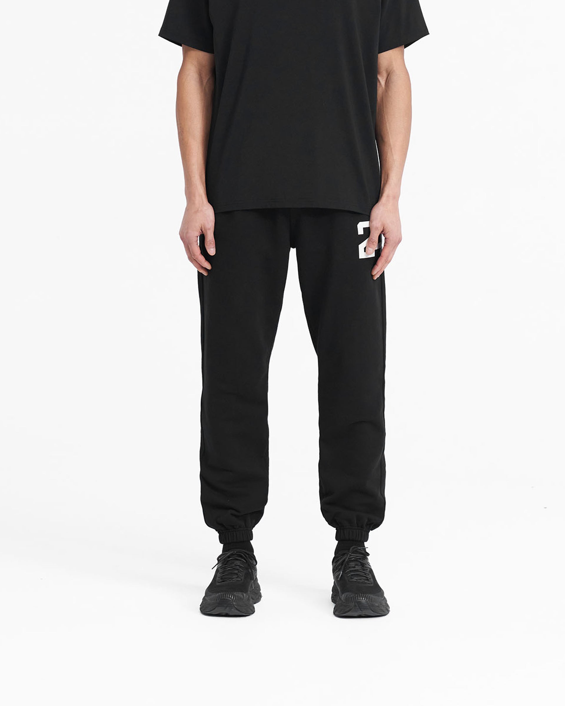 Man wearing black sweatpants on a plain white background | 247 Sweatpant in Black | Training joggers with elasticated cuffs and drawcord waist | 247 Pants | Represent Clo