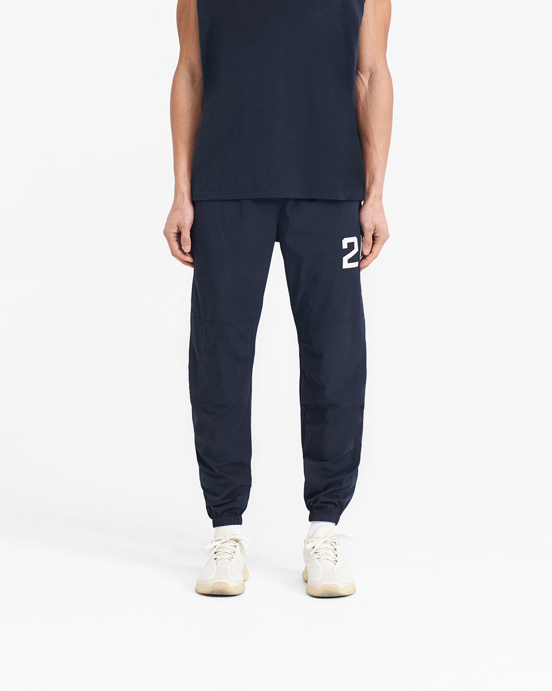 Man wearing navy pants on a plain white background | 247 Training Pant in Navy | Training pants with elasticated waistband and zip pockets | 247 Pants | Represent Clo