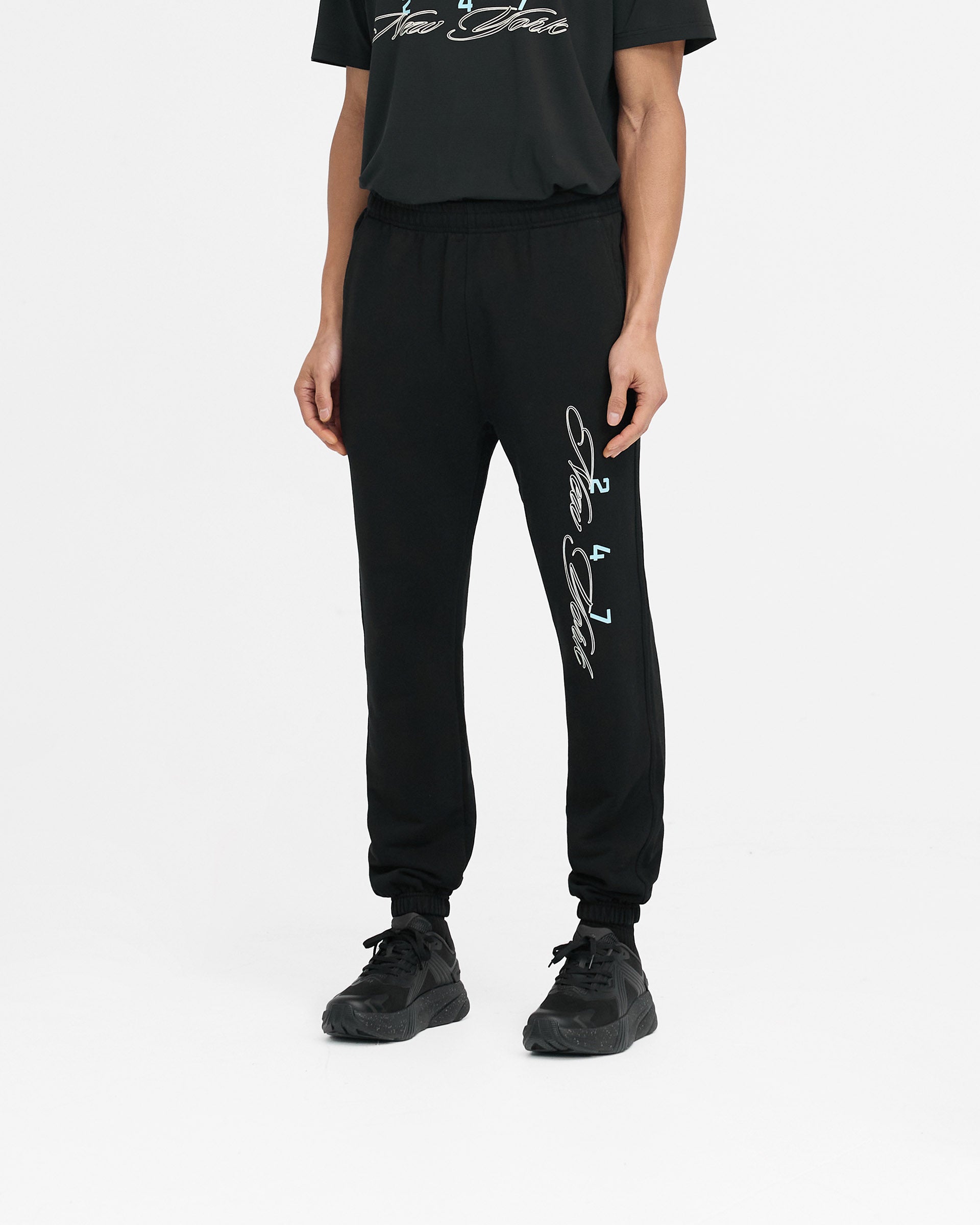 Man wearing black sweatpants on a plain white background | 247 New York Sweatpant in Black | Luxury joggers with elasticated cuffs and drawcord | 247 Pants | Represent Clo